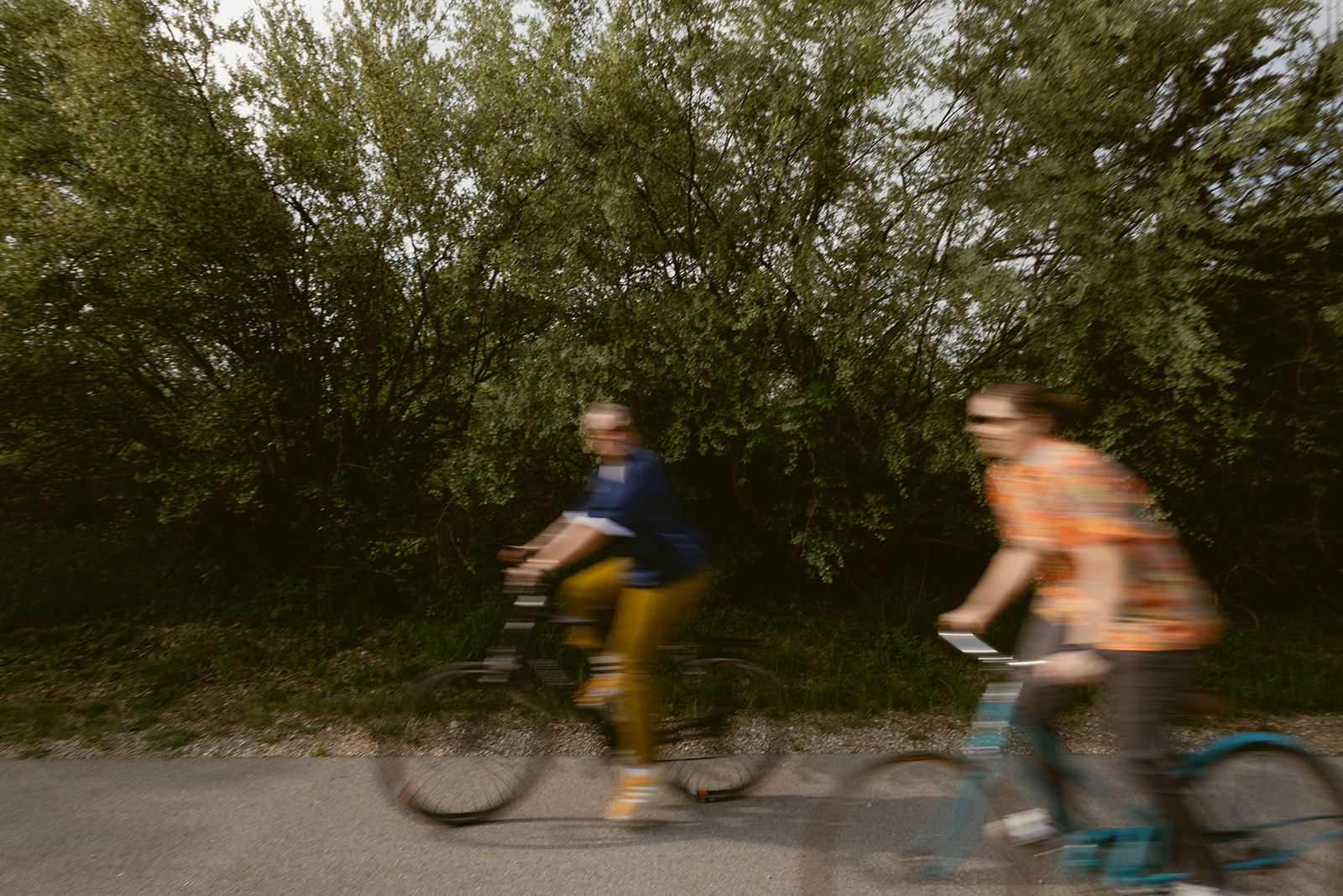 Two cyclists riding side-by-side along the paved Leelanau Trail under a lively green tree canopy
