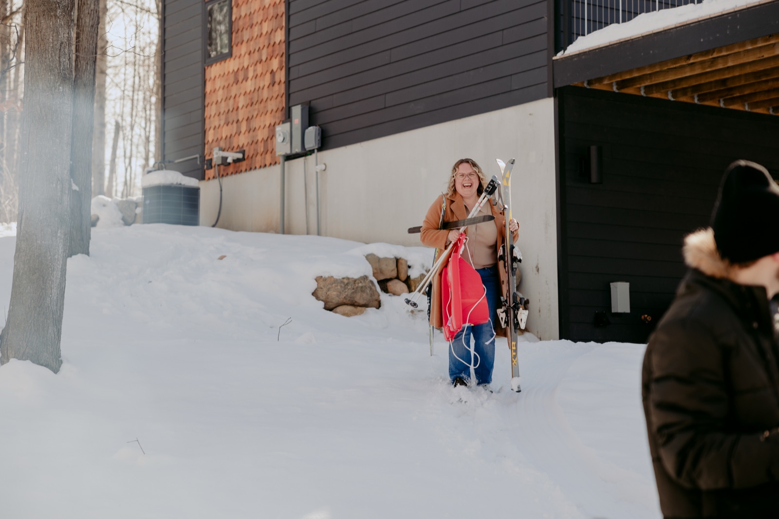 Guest carrying skis and a sled through deep snow outside a Roost North vacation rental in winter