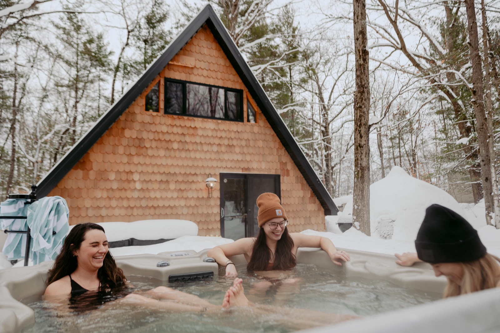 Three guests in a steaming hot tub surrounded by snow outside the A-Frame cabin near Traverse City