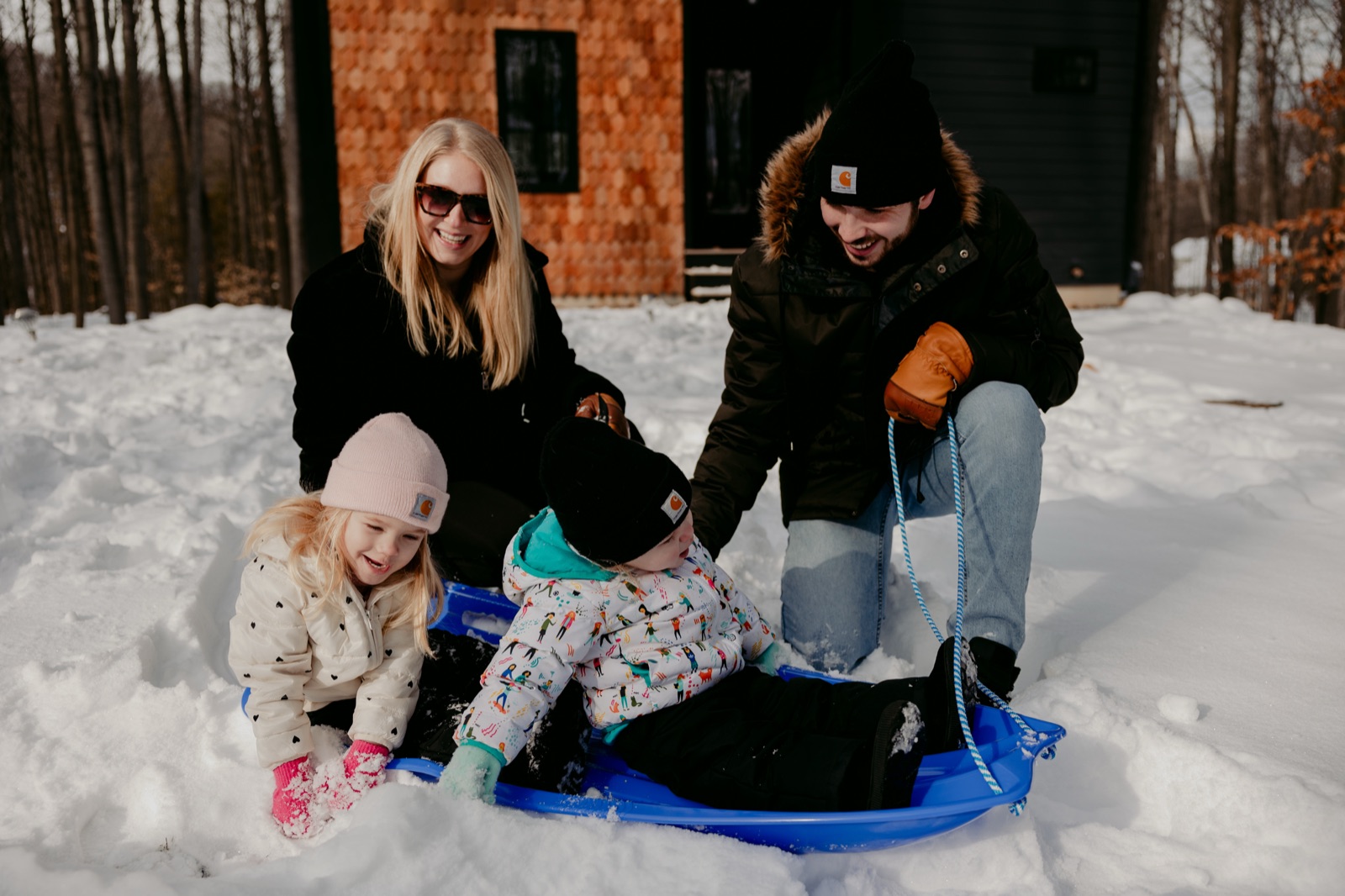 Family of four sledding together on a snowy day in front of a modern home near Traverse City